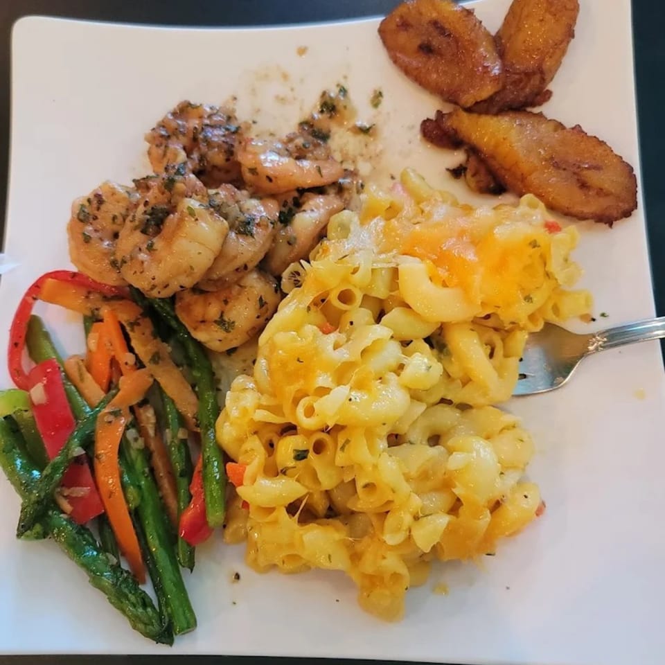 A Jamaican meal with seasoned shrimp, mac and cheese, sautéed vegetables, and fried plantains.