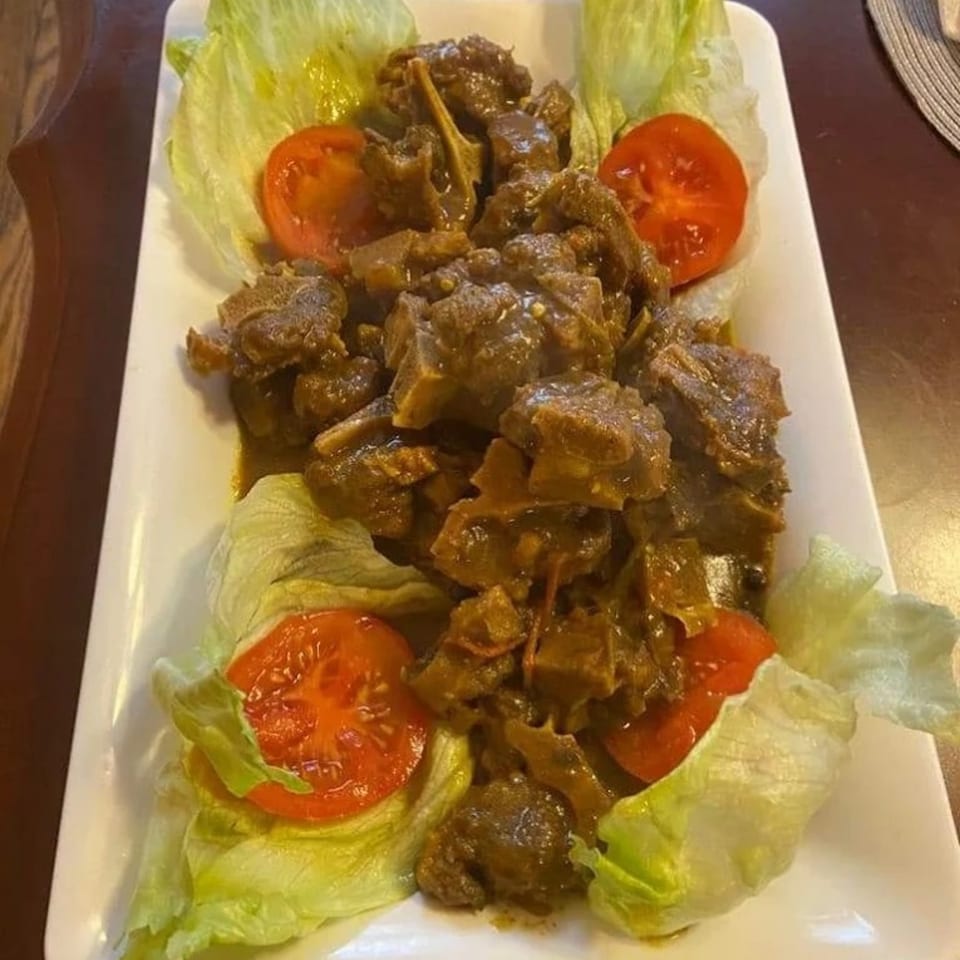 A white rectangular plate filled with Jamaican curry goat, garnished with lettuce and tomato slices.