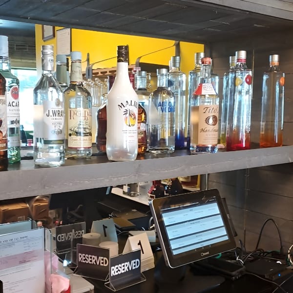 A bar shelf with various liquor bottles, a tablet, and "RESERVED" signs on the counter below.
