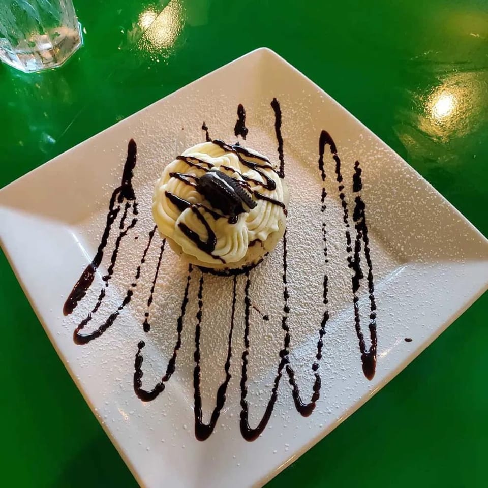 A dessert with white frosting, chocolate drizzle, and an Oreo cookie on a white plate.