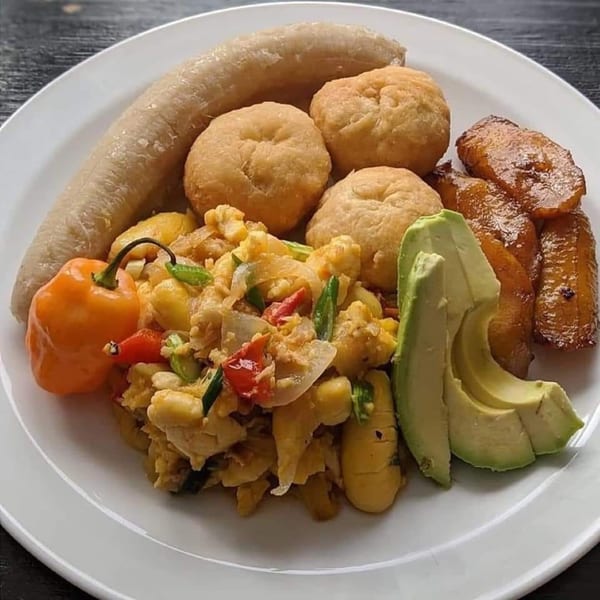 A Jamaican breakfast plate with ackee and saltfish, fried dumplings, boiled banana, plantains, and avocado.