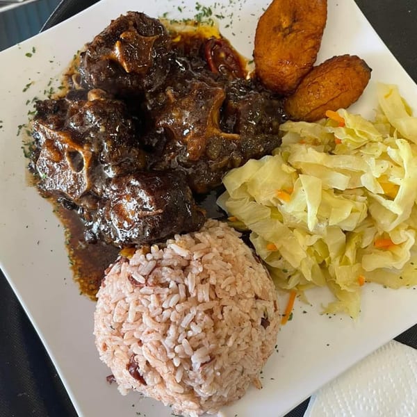 A plate of Jamaican oxtail stew, rice and peas, fried plantains, and steamed cabbage.
