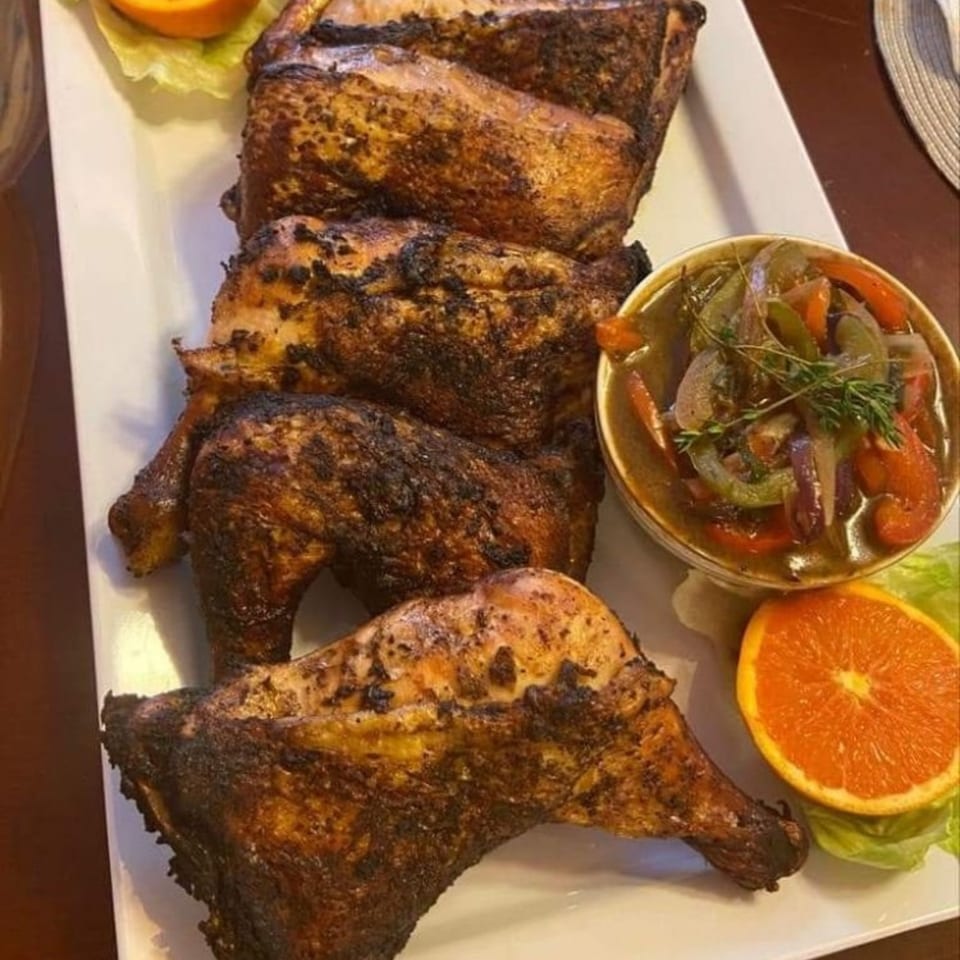 A platter of Jamaican jerk chicken with a side of stewed vegetables and orange slices.