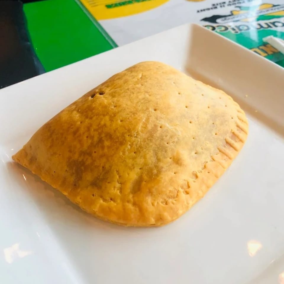A golden-brown Jamaican patty, a savory pastry, rests on a white rectangular plate.